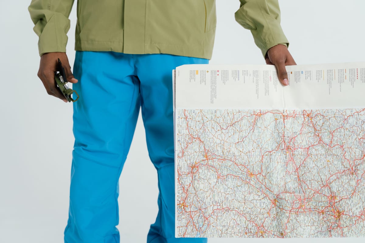 Man in outdoor attire holding a map and compass, prepared for exploration.